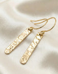 Flat lay of hammered gold filled bar dangle earrings, minimalist gold bar drop earrings on neutral background