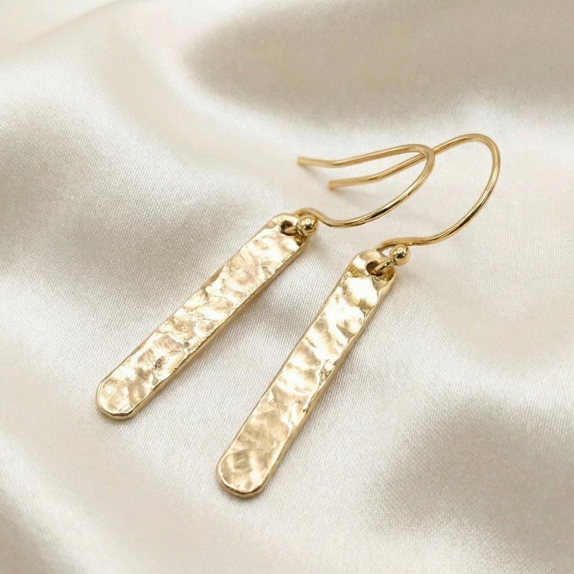 Flat lay of hammered gold filled bar dangle earrings, minimalist gold bar drop earrings on neutral background
