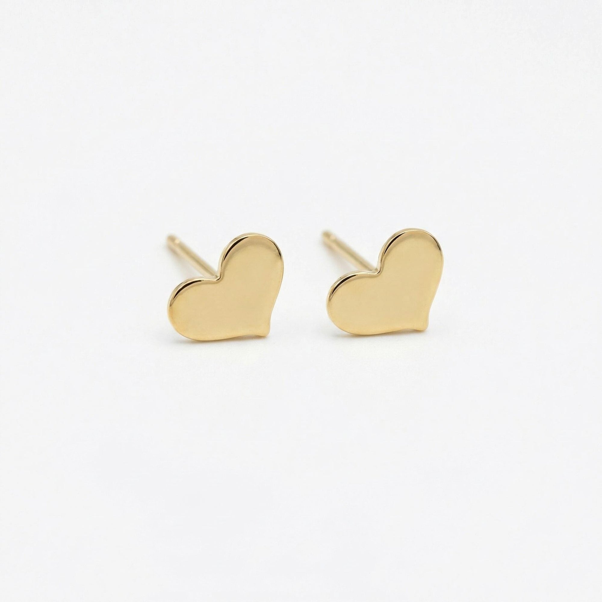 Tiny gold filled heart stud earrings displayed on a neutral flat lay background, minimalist handmade gold heart earrings for everyday wear