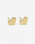 Tiny gold filled heart stud earrings displayed on a neutral flat lay background, minimalist handmade gold heart earrings for everyday wear