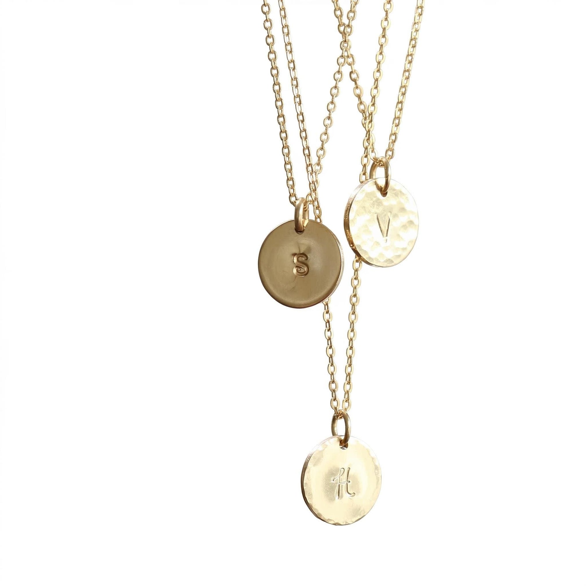Three gold necklaces with hammered disc pendants, each featuring a different initial: S, V, and H.