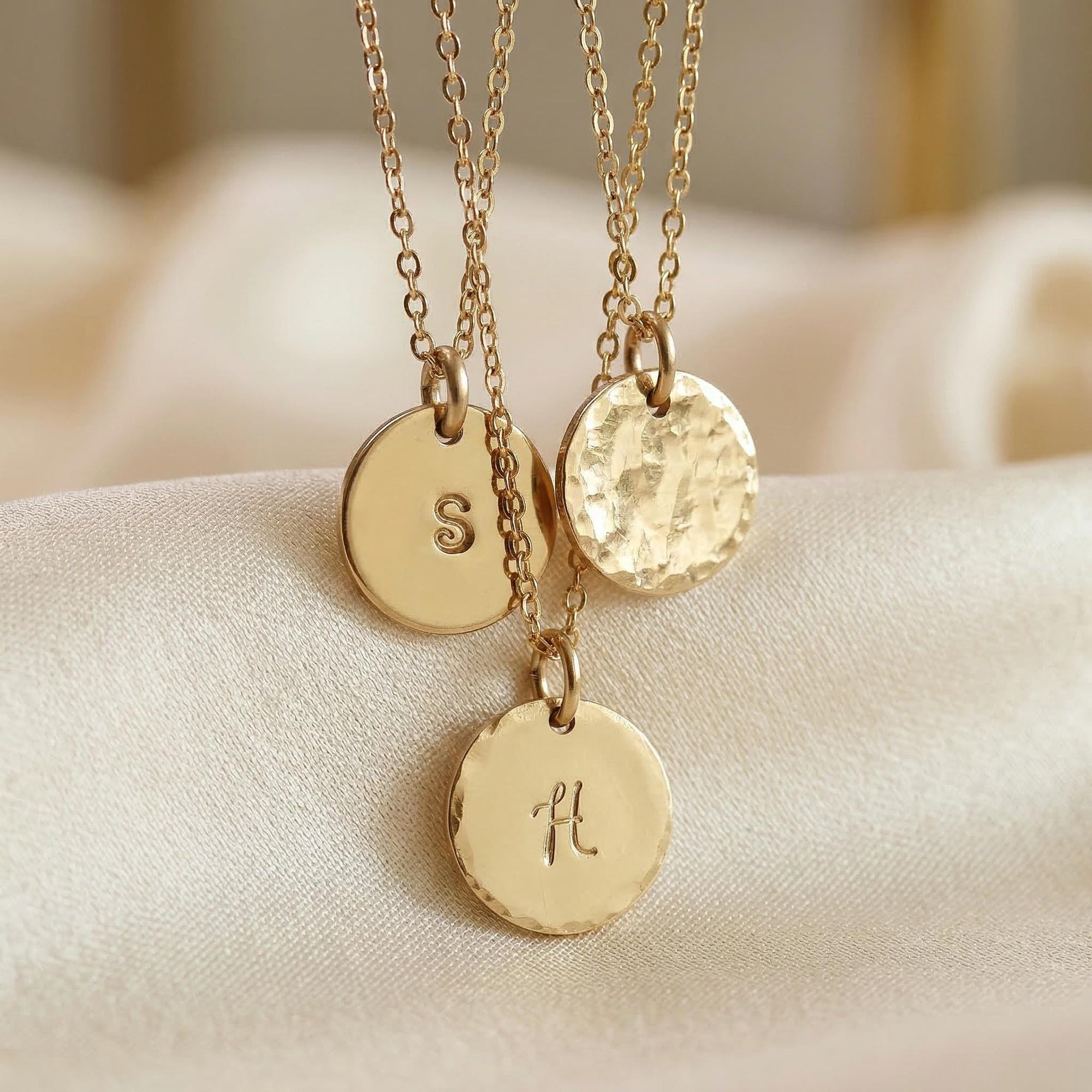Three gold necklaces with hammered disc pendants, each featuring a different initial: S, V, and H.