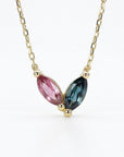 A delicate gold chain necklace with a pendant featuring two marquise-shaped tourmaline gemstones. The gemstone on the left is pink, and the gemstone on the right is a dark green.