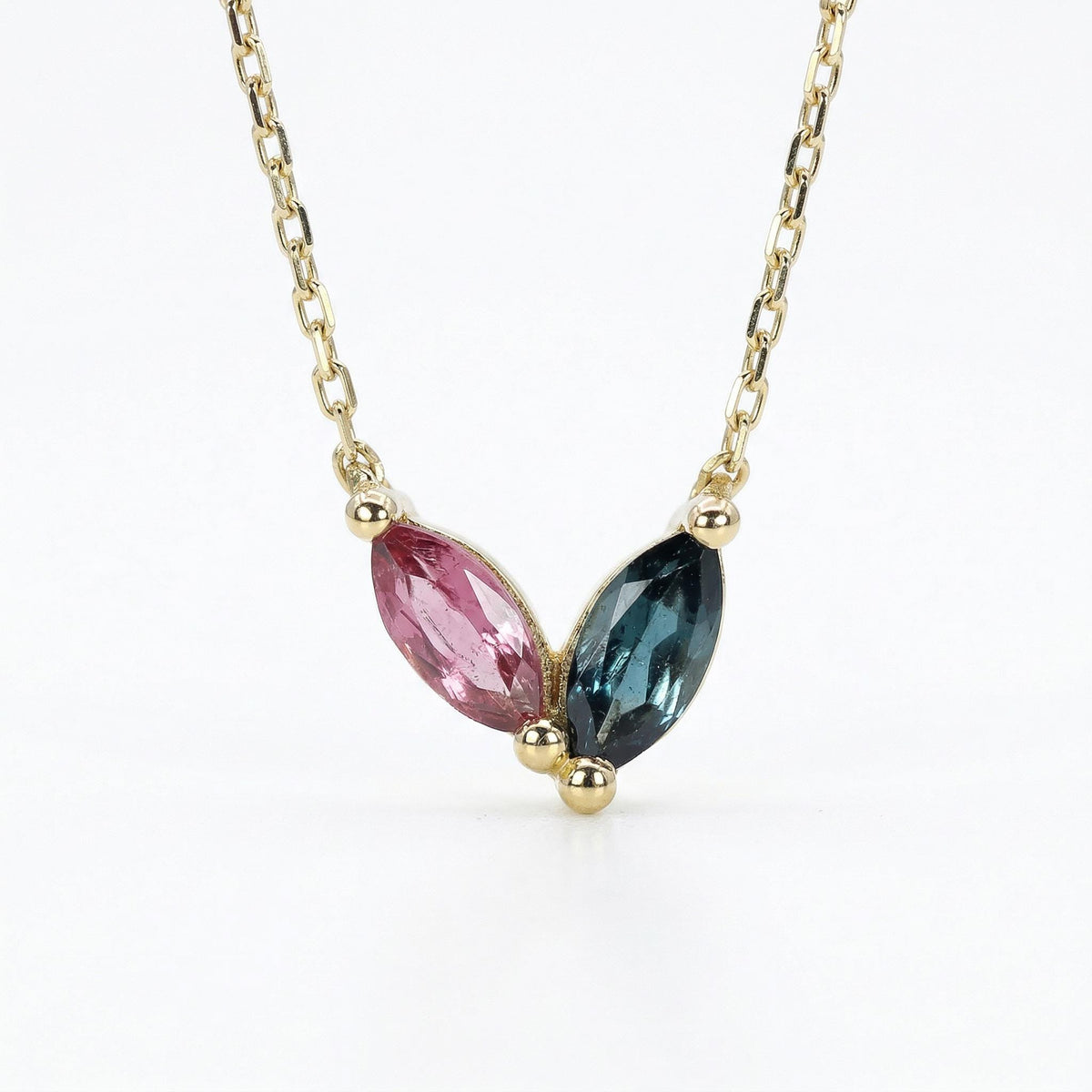 A delicate gold chain necklace with a pendant featuring two marquise-shaped tourmaline gemstones. The gemstone on the left is pink, and the gemstone on the right is a dark green.