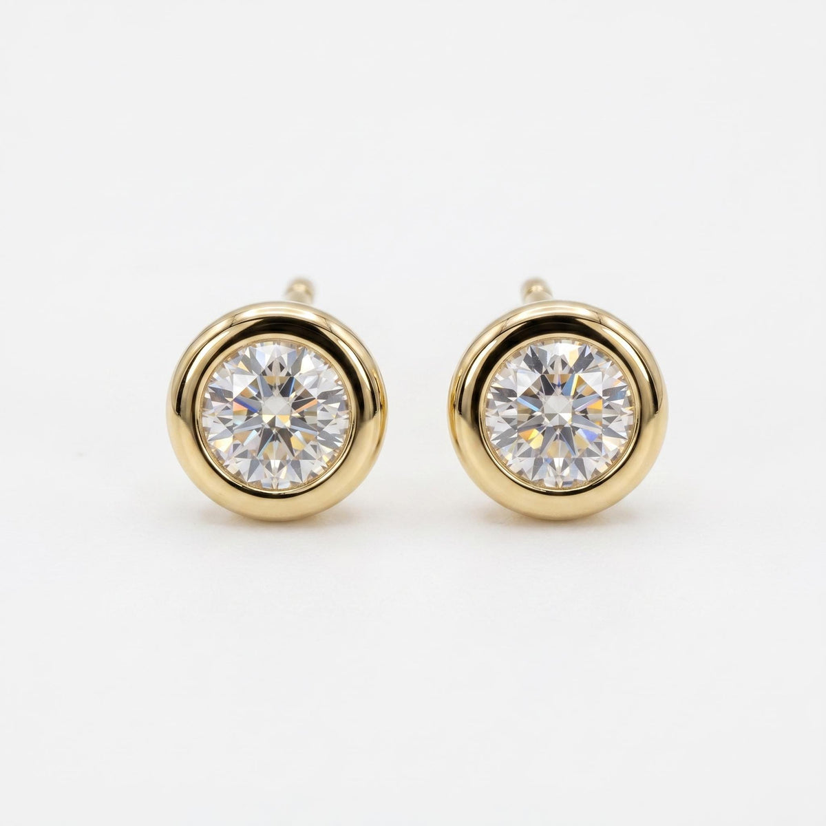 A pair of round, faceted clear gemstone stud earrings, each set in a smooth, polished gold bezel.