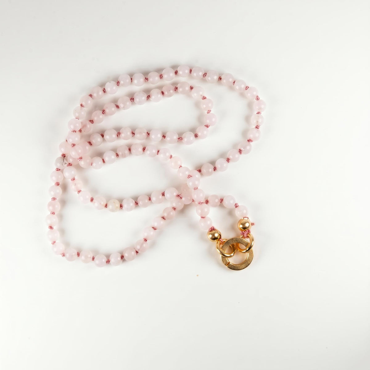 A light pink beaded necklace with a gold-colored clasp, laid flat on a white surface.
