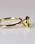 A side view of a gold ring with a bezel-set, cushion-cut green peridot gemstone on a white surface.