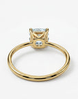 A gold ring with a light blue cushion-cut gemstone is shown from a slightly elevated side view, highlighting the four prongs and the open basket setting.