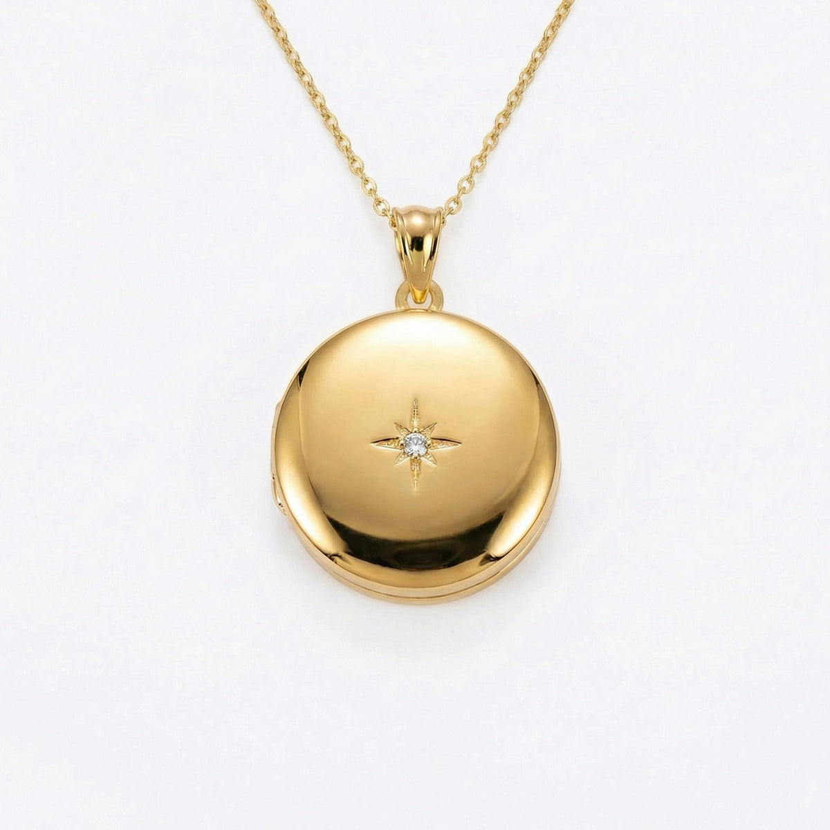 A round gold locket with a small, clear gem in the center, set in a starburst design, hangs from a delicate gold chain.
