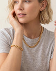 A person wearing a gray t-shirt, a gold Cuban chain necklace, and a matching gold Cuban chain bracelet.