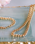 A gold Cuban chain bracelet and a gold Cuban chain necklace lie on a light blue and gold tray.