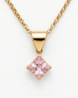 A gold chain necklace with a square, blush-pink gemstone pendant, set in a gold bezel, is displayed against a white background.