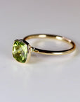 An angled view of a gold ring with a bezel-set, cushion-cut green peridot gemstone on a white surface.