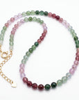 A necklace of faceted pink, green, and purple ombre beads with a gold-colored clasp and extender chain is displayed on a white background.