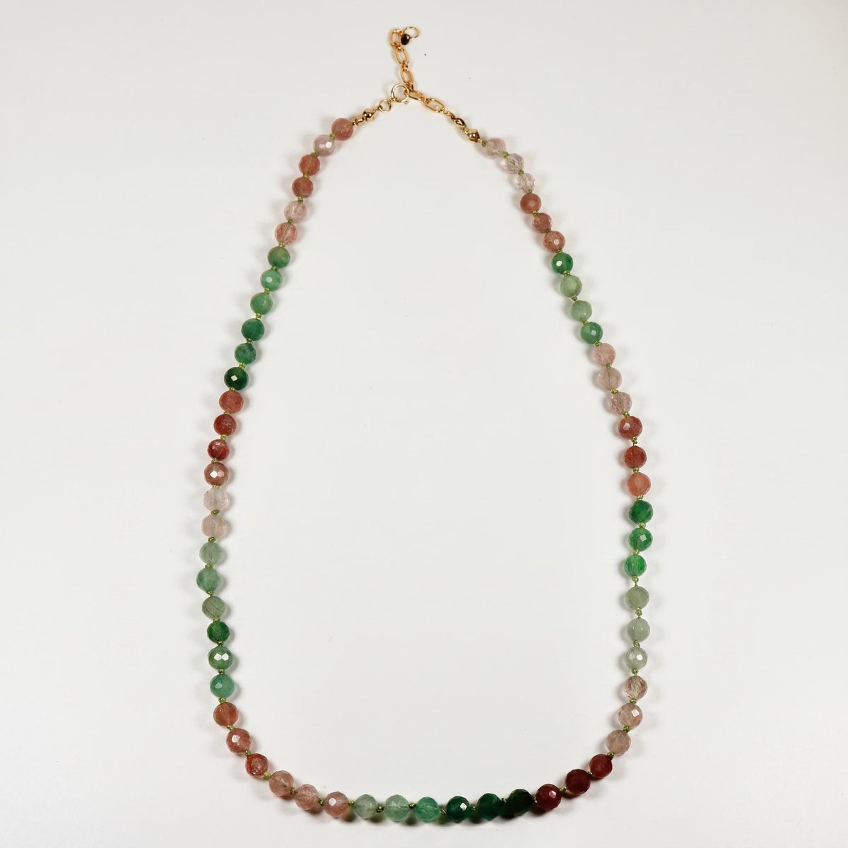 A necklace of faceted pink, green, and purple ombre beads with a gold-colored clasp is laid out straight on a white surface.