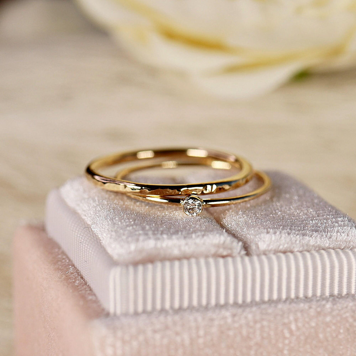 Two thin gold rings, one smooth with a small diamond and one hammered, rest on a pink velvet ring box.