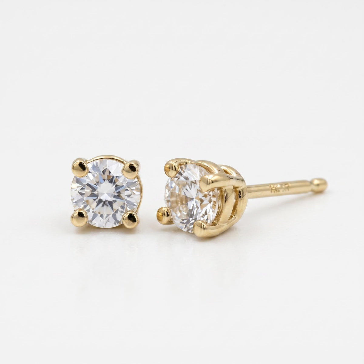 A pair of round, faceted white sapphire stud earrings in four-prong gold settings, viewed from a slight angle on a white background.