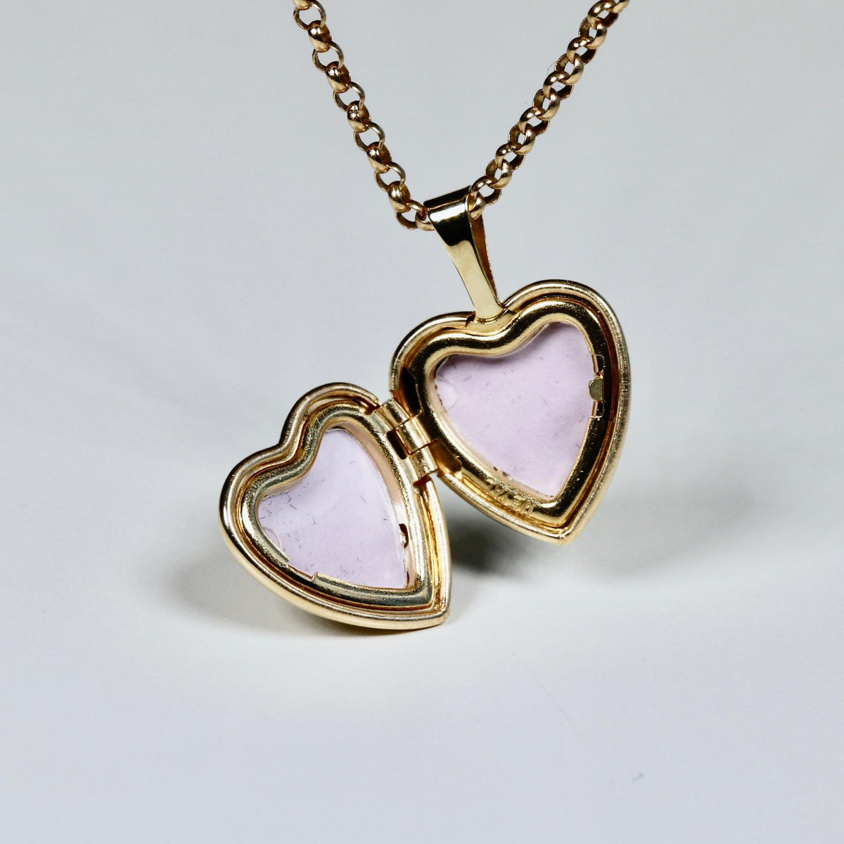 An open gold heart-shaped locket on a gold chain, revealing two pink-lined compartments.