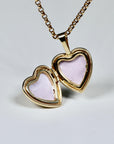 An open gold heart-shaped locket on a gold chain, revealing two pink-lined compartments.