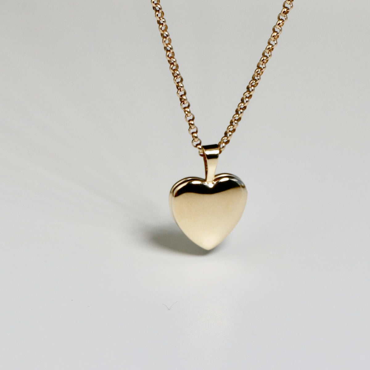 A gold heart-shaped locket on a gold chain, against a plain white background.