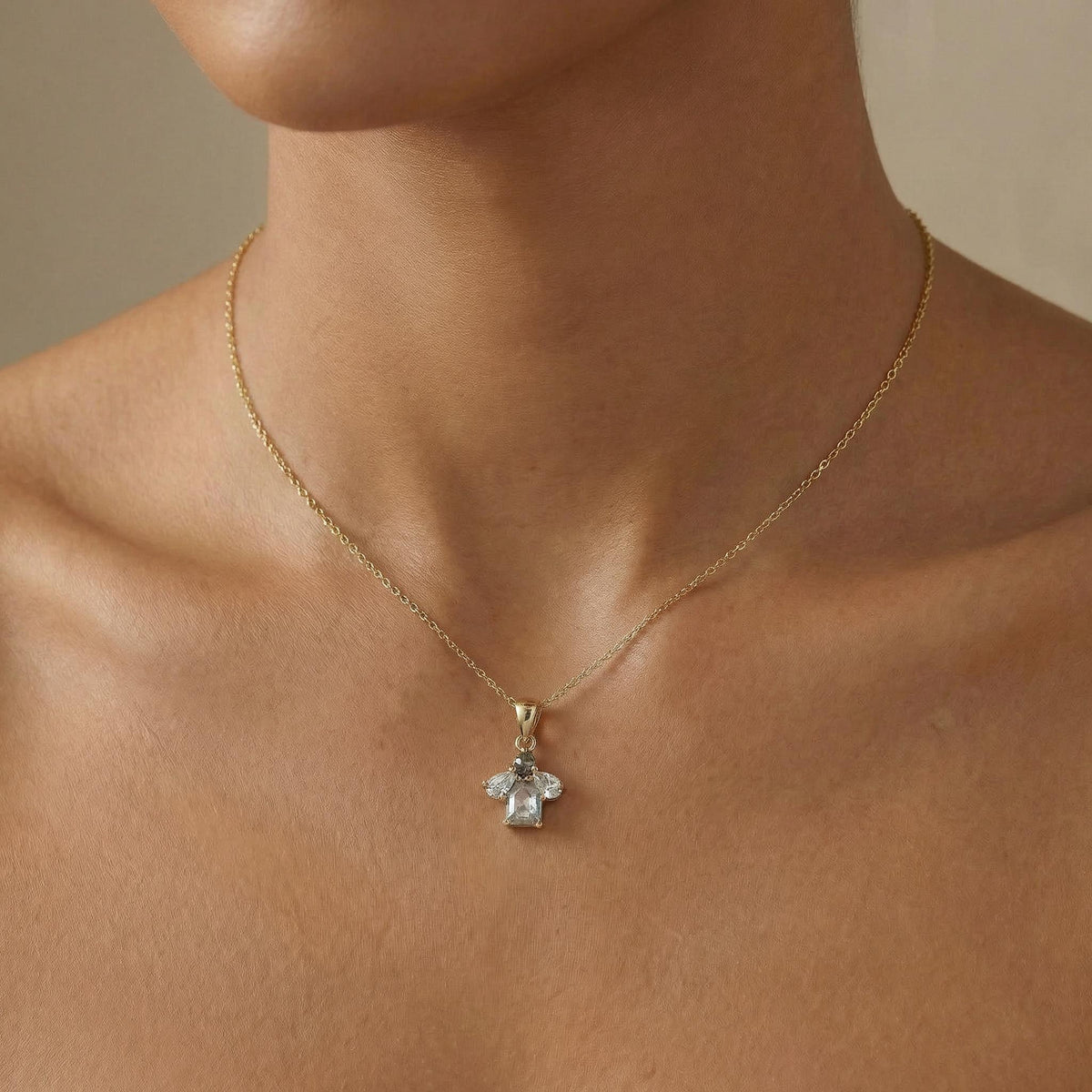 A gold chain necklace with a cluster pendant featuring a rectangular diamond flanked by two pear-shaped diamonds, worn on a person's chest.