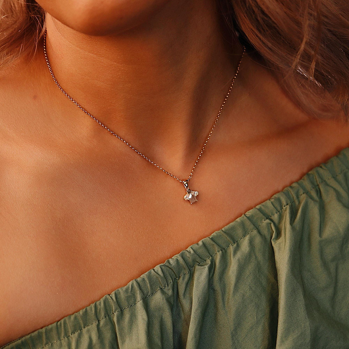 A rose gold chain necklace with a small cluster pendant featuring a rectangular diamond and two pear-shaped diamonds, worn on a person&amp;