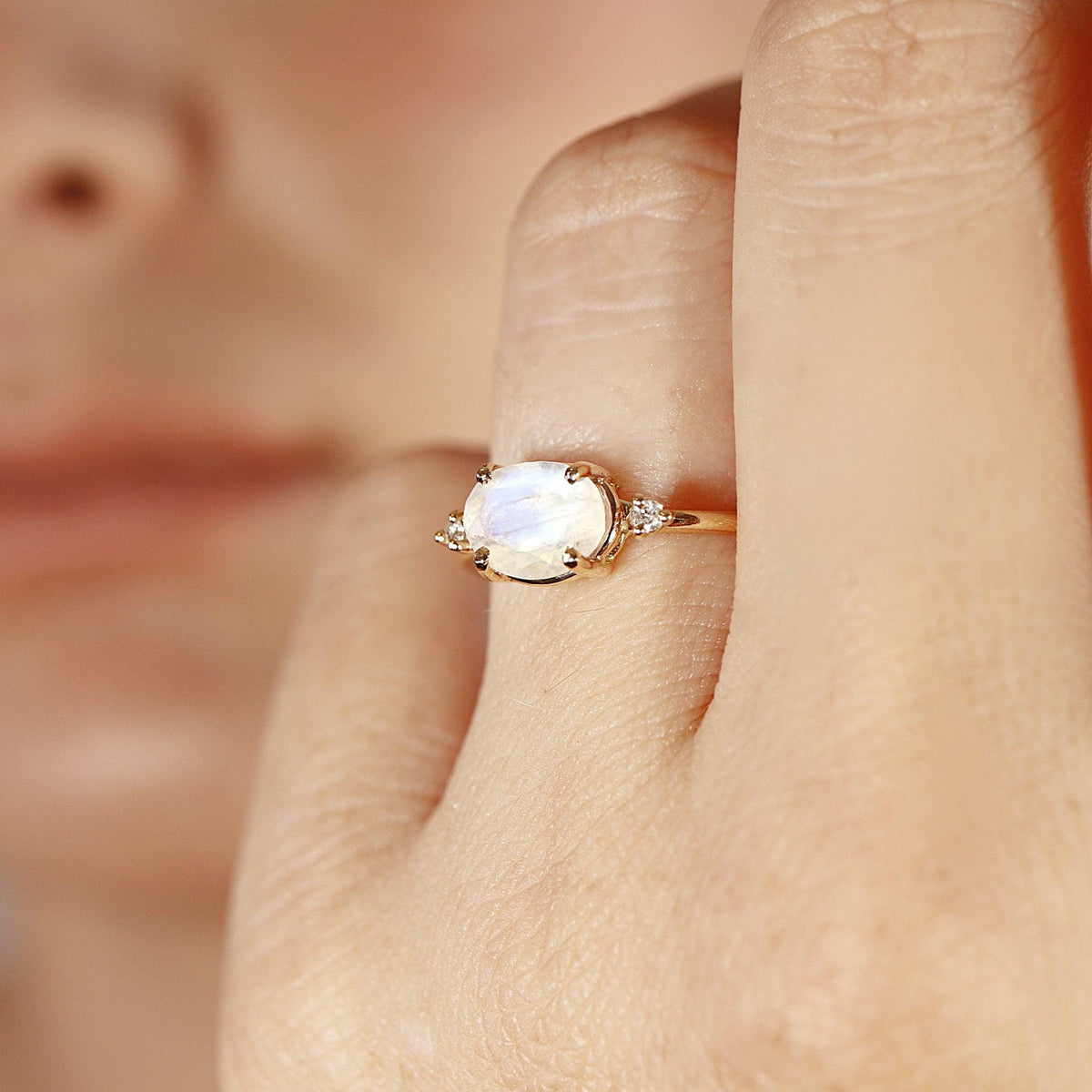 A gold ring with an oval moonstone and two small diamonds on each side, worn on a person&amp;