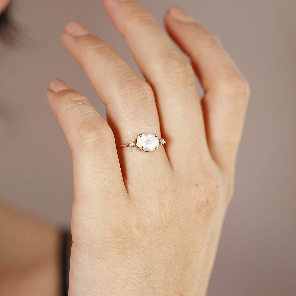 A gold ring with an oval moonstone and two small diamonds on each side, worn on a person&amp;