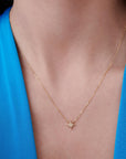 A gold chain necklace with a small, flat, eight-point star pendant, encrusted with tiny clear stones, worn by a person in a blue top.