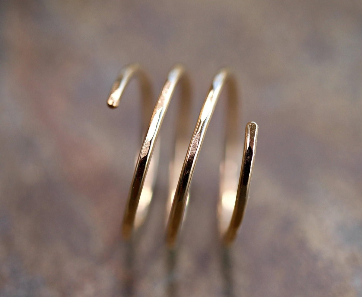 A gold-colored, three-coil spiral ring with hammered texture is shown on a blurred brown background.