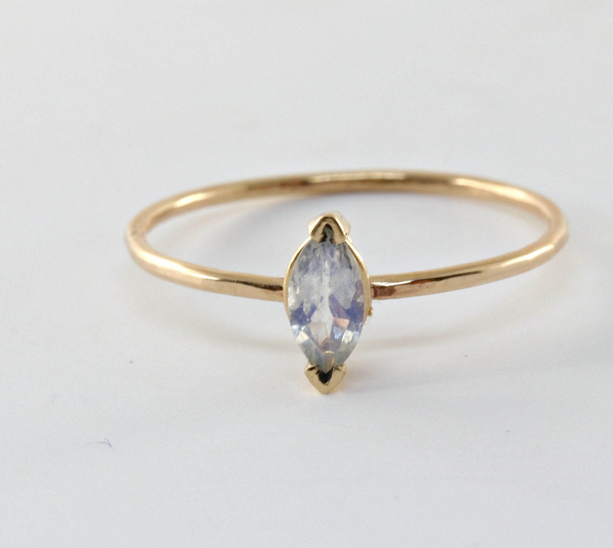 A thin gold ring with a marquise-cut, iridescent white gemstone set horizontally in a bezel setting.