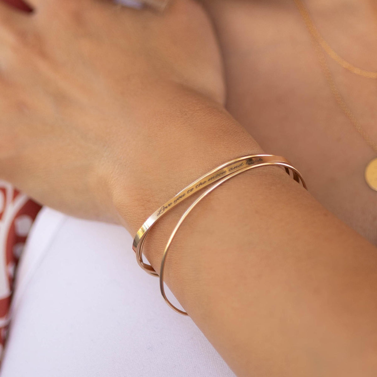 A gold-colored open cuff bracelet with the engraved text &amp;quot;Love you to the moon and back&amp;quot; is worn on a person&amp;