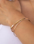 A gold-colored open cuff bracelet with the engraved text "Love you to the moon and back" is worn on a person&