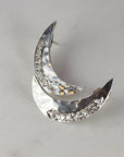 Close-up of two silver crescent moon earrings with hammered texture and embedded stones resting on a light marble background.