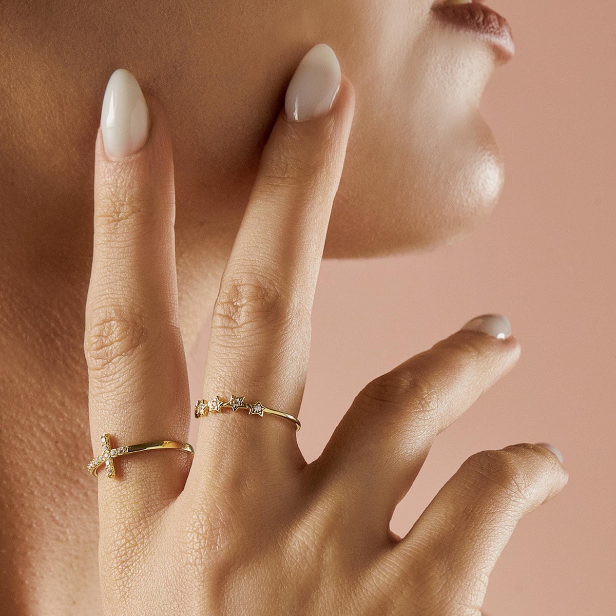 A person's hand with two gold rings: one with a diamond-studded cross and another with five diamond-studded stars.