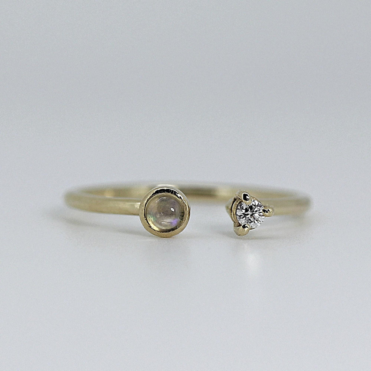 A thin gold open cuff ring with a round, iridescent opal on the left and a small, clear diamond in a prong setting on the right.
