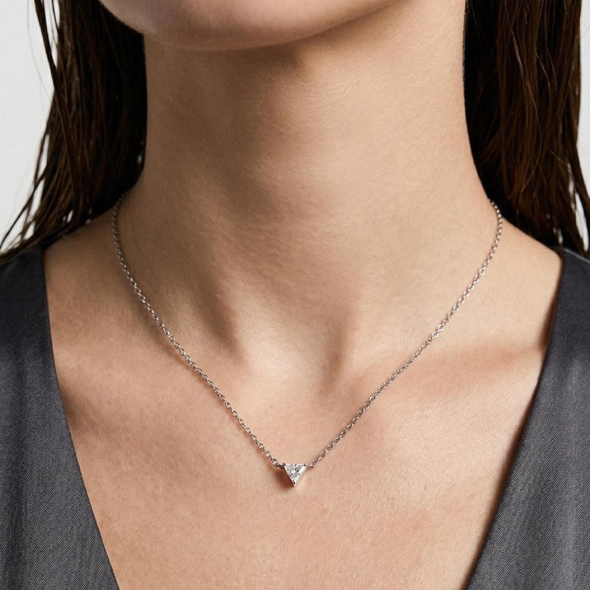 A person wearing a delicate silver chain necklace with a small triangle gemstone pendant against a grey top.