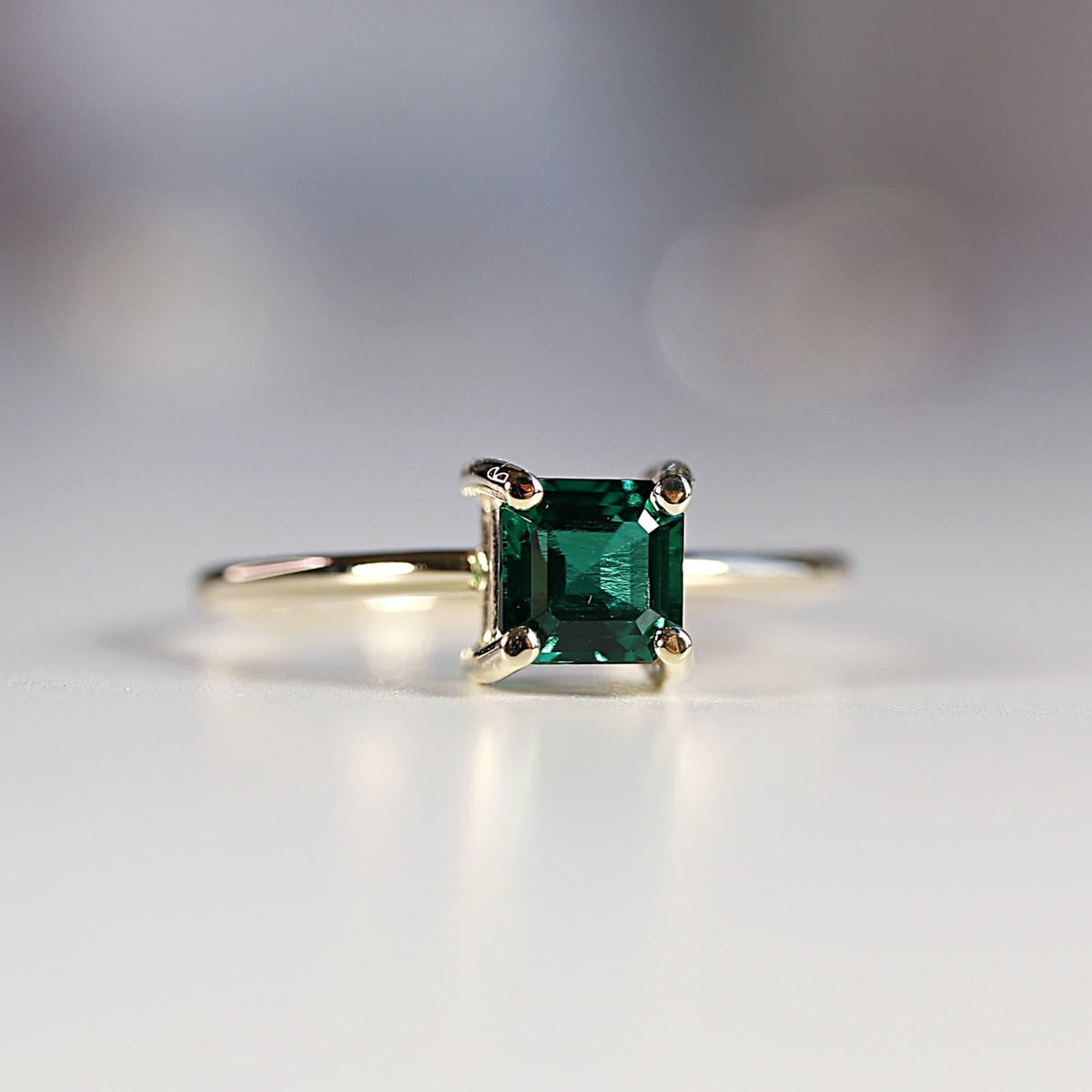 Top-down view of a square green gemstone set in gold on a thin band against a neutral background.