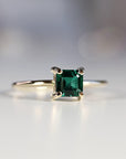 Top-down view of a square green gemstone set in gold on a thin band against a neutral background.