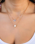 Front view of a person wearing a layered rose gold necklace set featuring an initial-engraved heart charm and a pearl pendant.