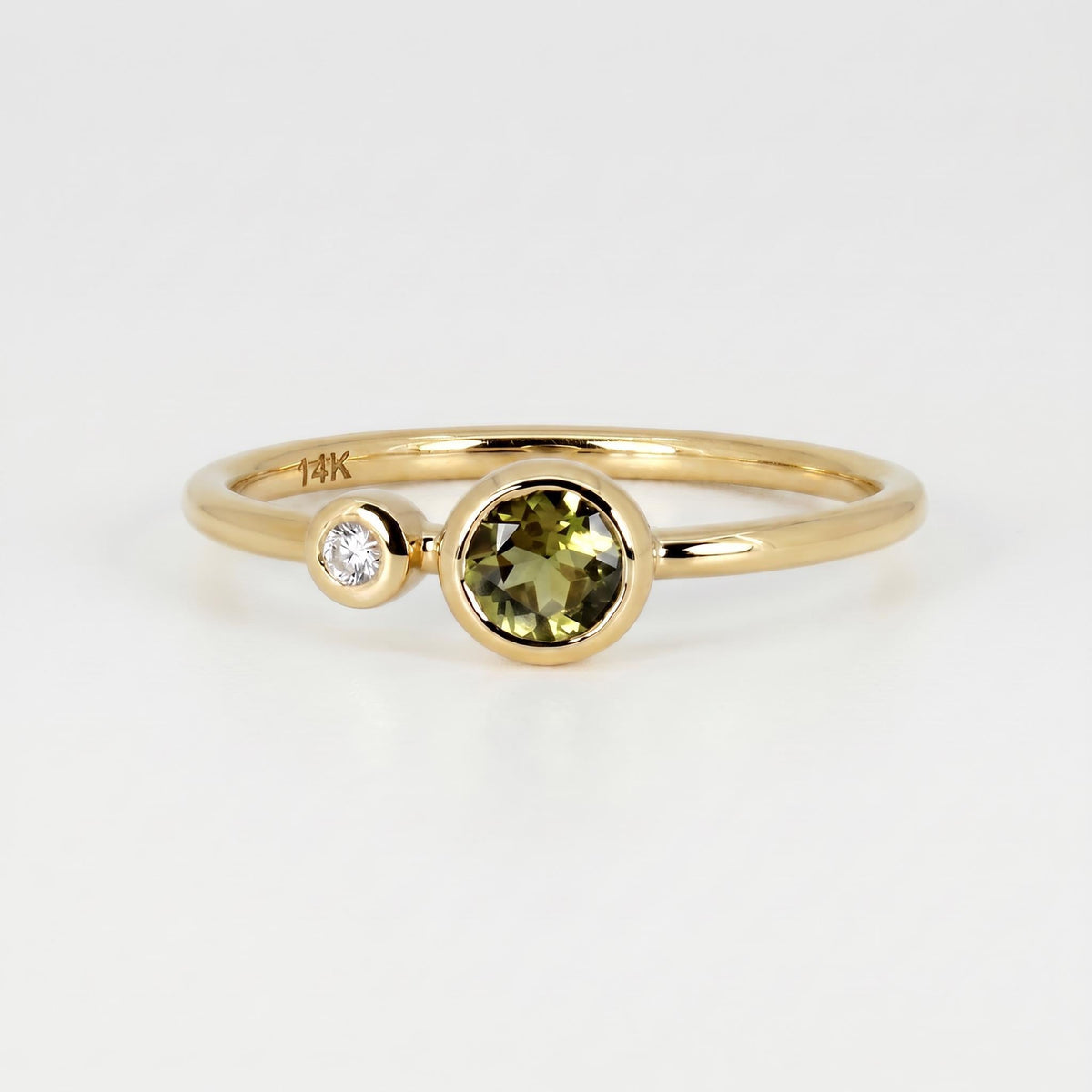 A yellow gold ring featuring a bezel-set green tourmaline and a smaller bezel-set diamond side-by-side, with the 14K stamp visible on the inner band.