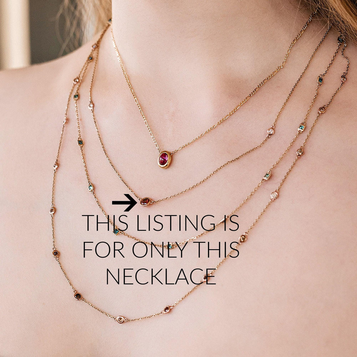 A close-up of a person's chest and neck shows four layered gold necklaces, with an arrow pointing to the second shortest necklace, which has a single red oval gem, and text that reads: "THIS LISTING IS FOR ONLY THIS NECKLACE."