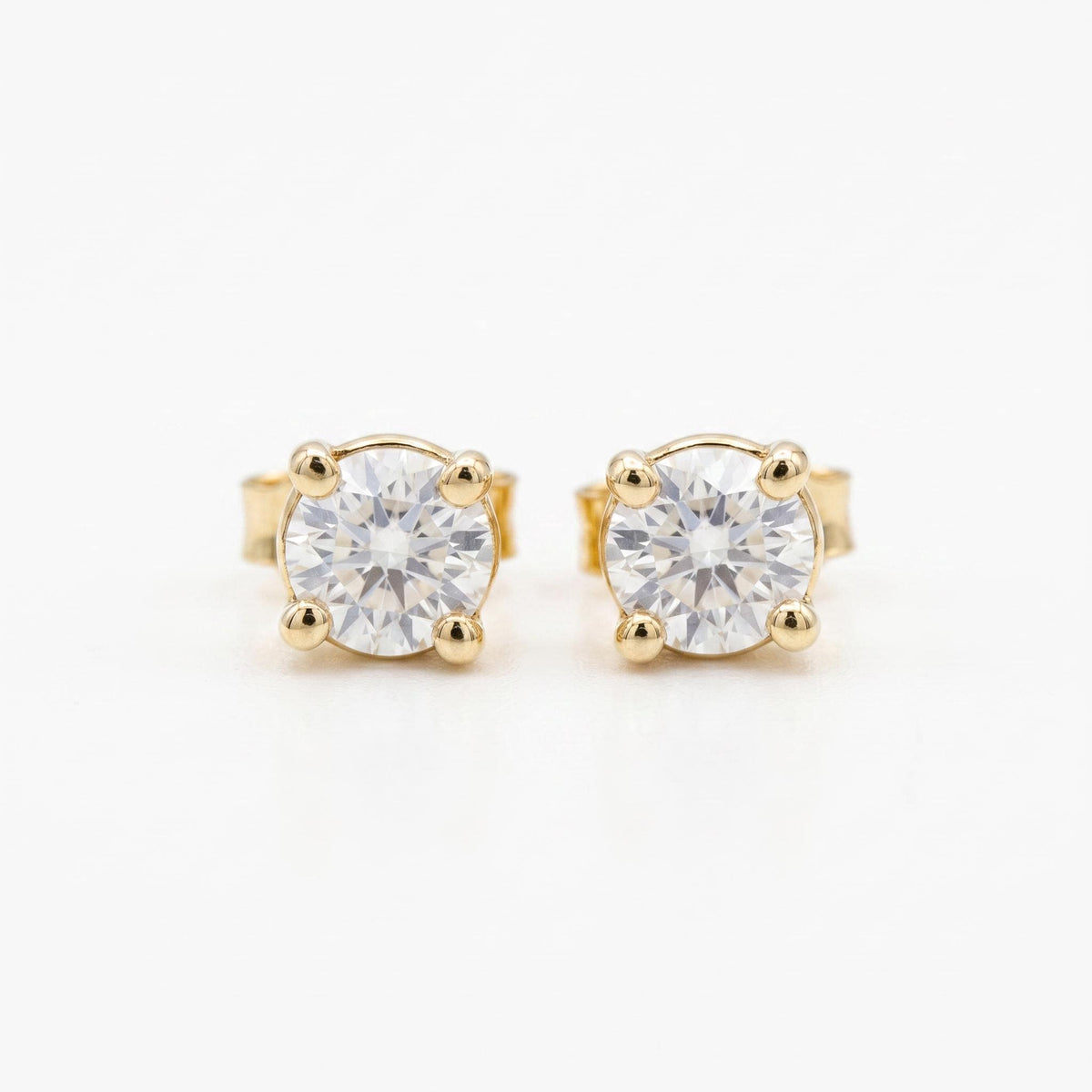 A pair of round, faceted white sapphire stud earrings in four-prong gold settings, viewed from the front on a white background.