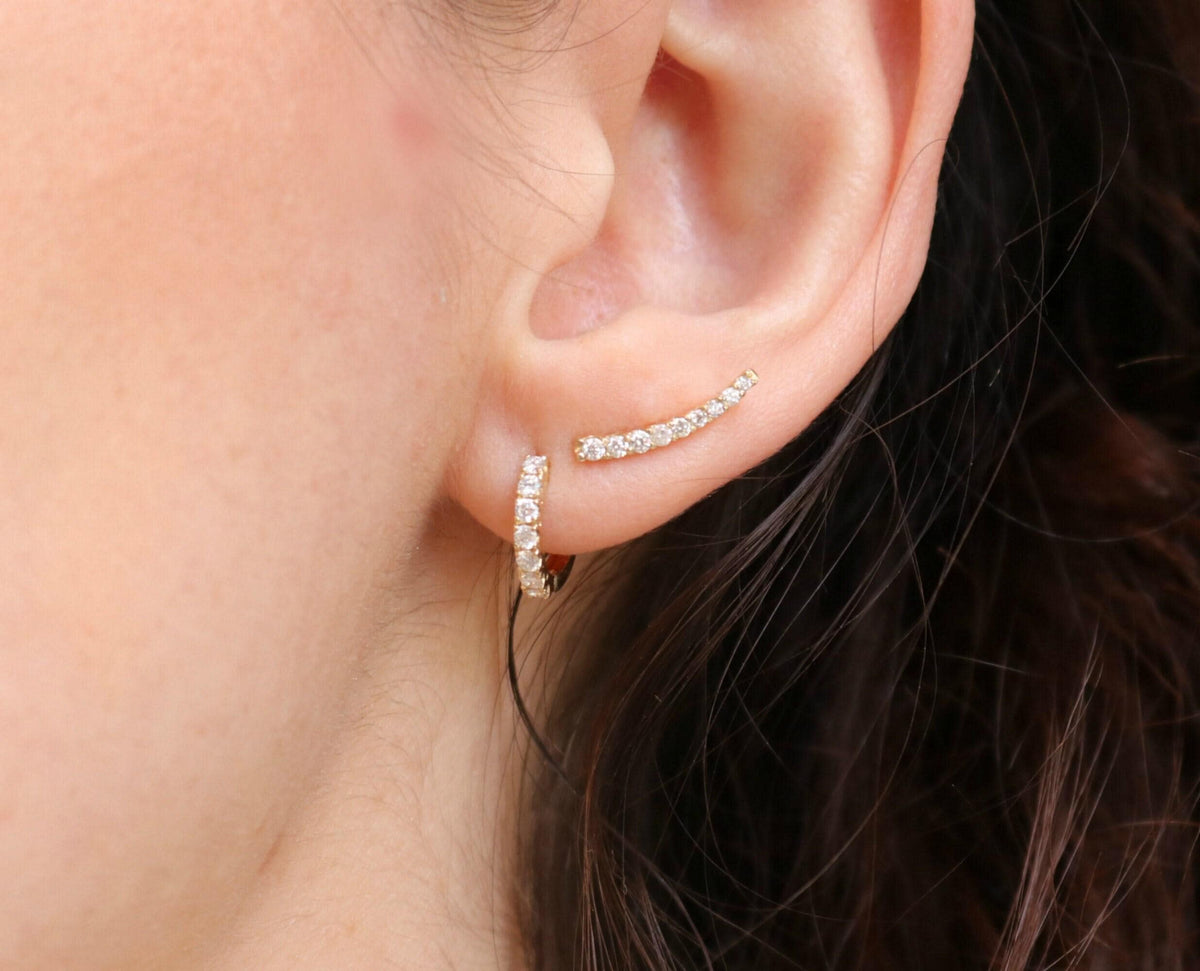 A gold huggie hoop earring with diamonds is worn in the lower lobe of an ear, with a curved diamond ear climber in the upper lobe.