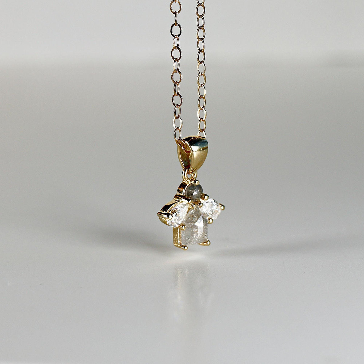 A close-up of a gold chain necklace with a cluster pendant featuring a gray round diamond, a gray rectangular diamond, and two clear pear-shaped diamonds.
