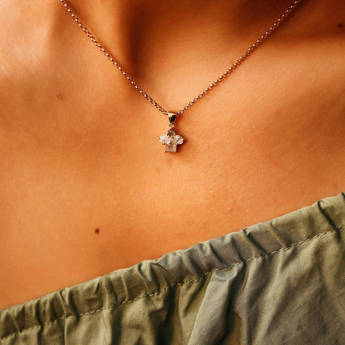 A rose gold chain necklace with a small cluster pendant featuring a rectangular diamond and two pear-shaped diamonds, worn on a person&amp;