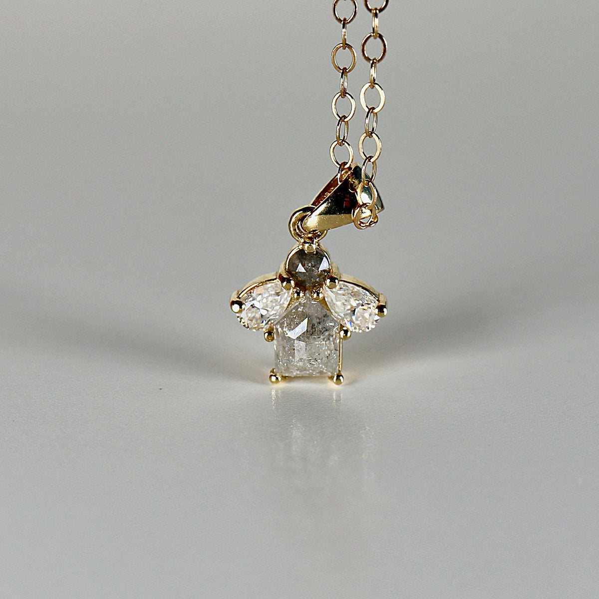 A close-up of a gold chain necklace with a cluster pendant featuring a gray round diamond, a gray rectangular diamond, and two clear pear-shaped diamonds.