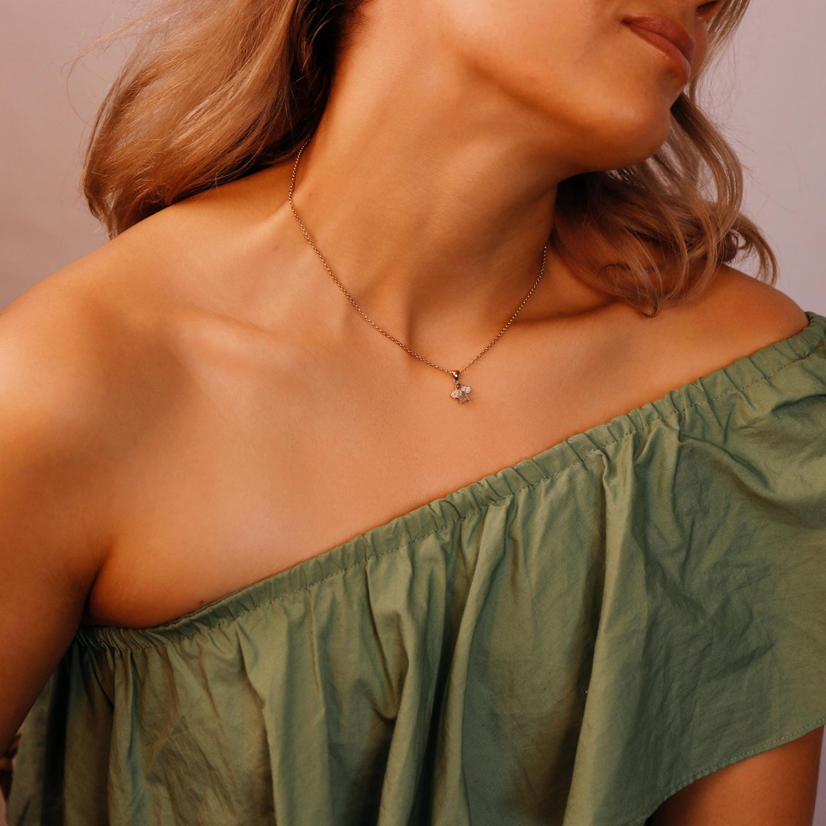 A gold chain necklace with a small cluster pendant featuring a rectangular diamond and two pear-shaped diamonds, worn on a person&amp;
