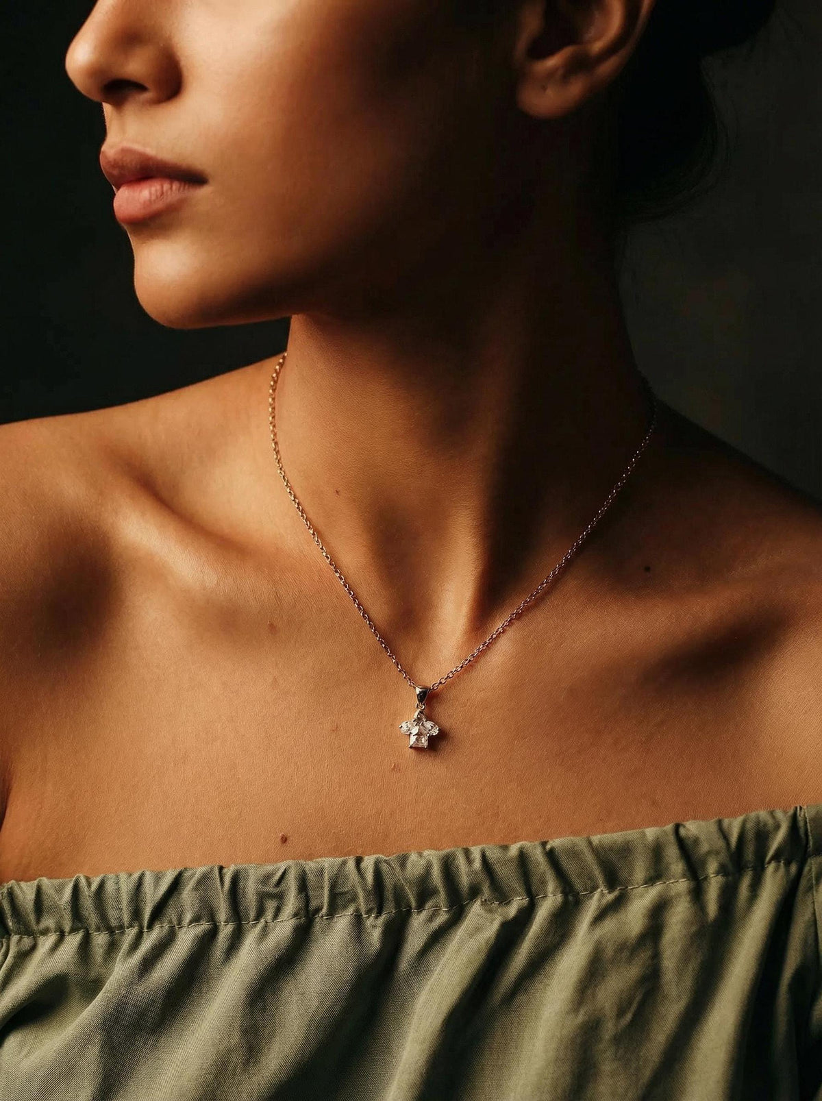 A gold chain necklace with a small cluster pendant featuring a rectangular diamond and two pear-shaped diamonds, worn on a person&amp;