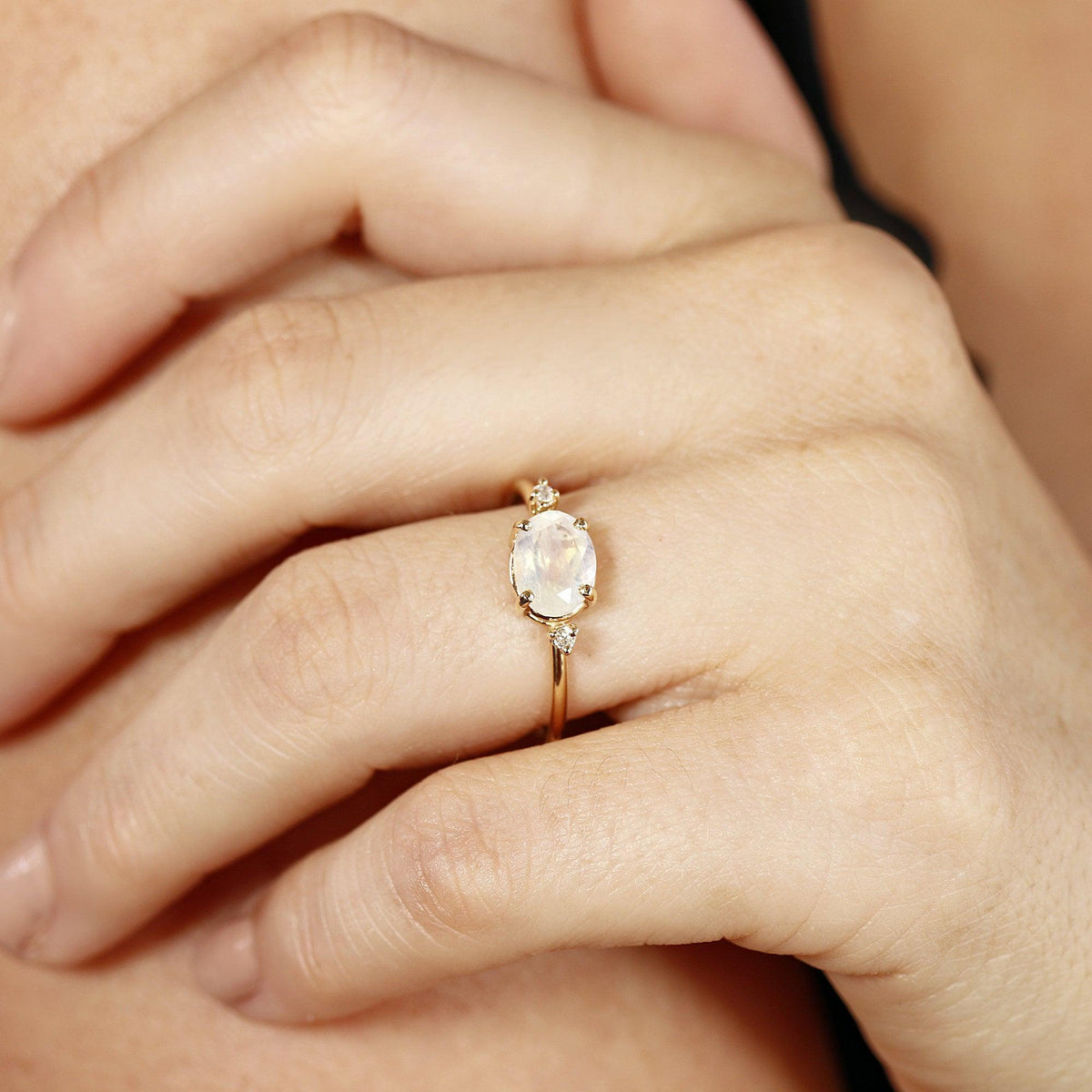 A gold ring with an oval moonstone and two small diamonds on each side, worn on a person&amp;